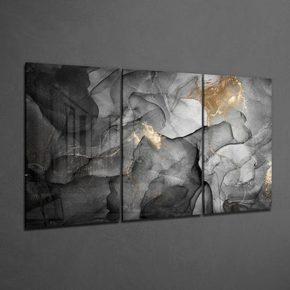 Three-panel gray glass wall art with black, white, and gold abstract fluid patterns displayed on gray wall.