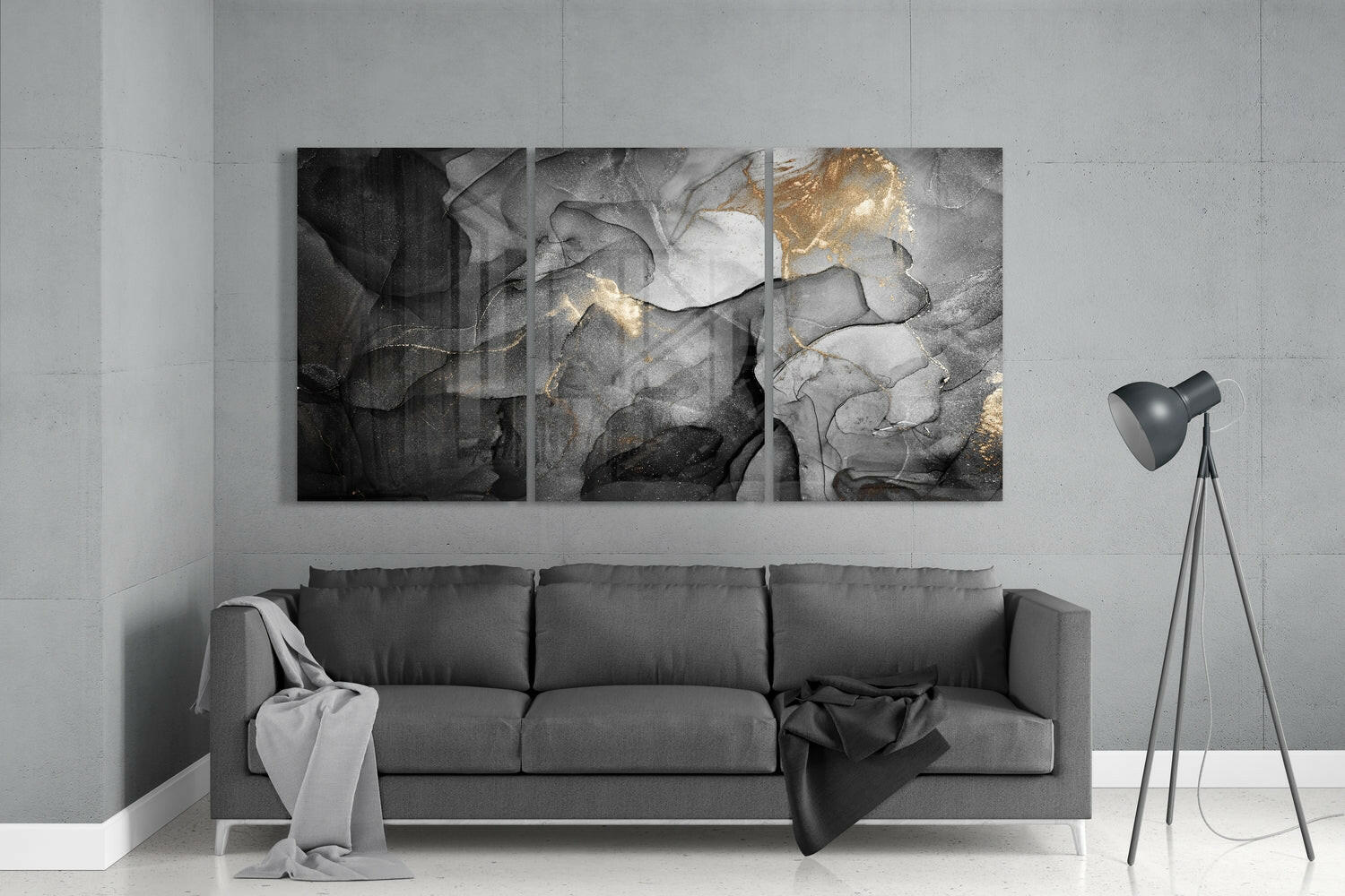 Three-panel abstract glass wall art with black, gray, and gold marbling hung above a gray sofa in a minimalist interior.
