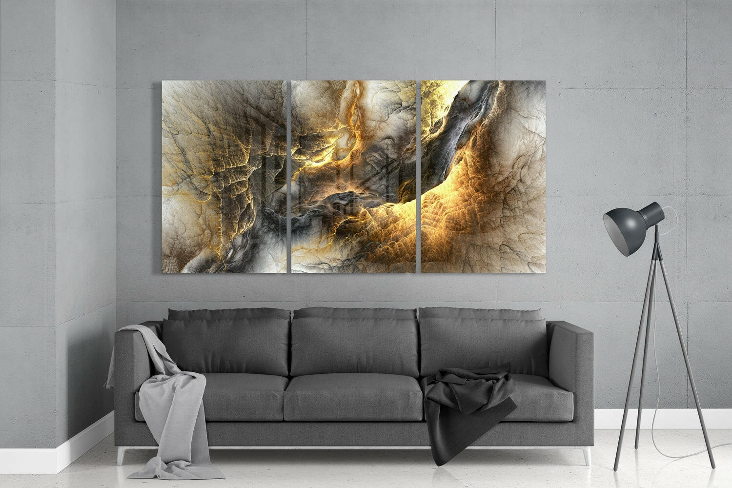 Three-panel yellow and gold glass wall art with abstract molten patterns displayed above gray sofa in minimalist room setting.