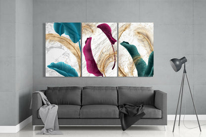 Three glass panels with teal, magenta, and green painted leaves over gold feather designs displayed above a gray sofa in a modern interior.