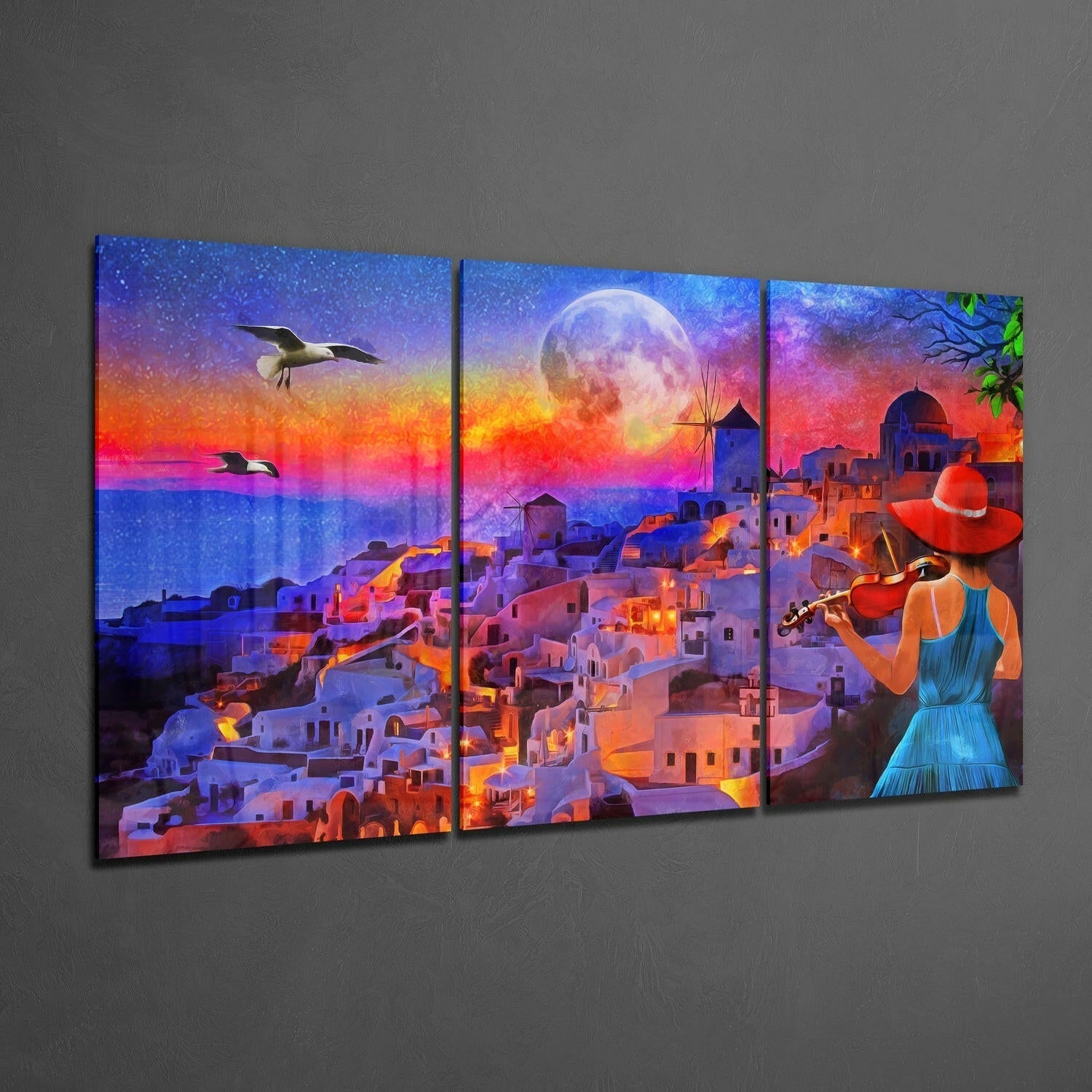 Three-panel glass wall art displaying a colorful Mediterranean coastal village at sunset with a woman playing violin in the foreground.