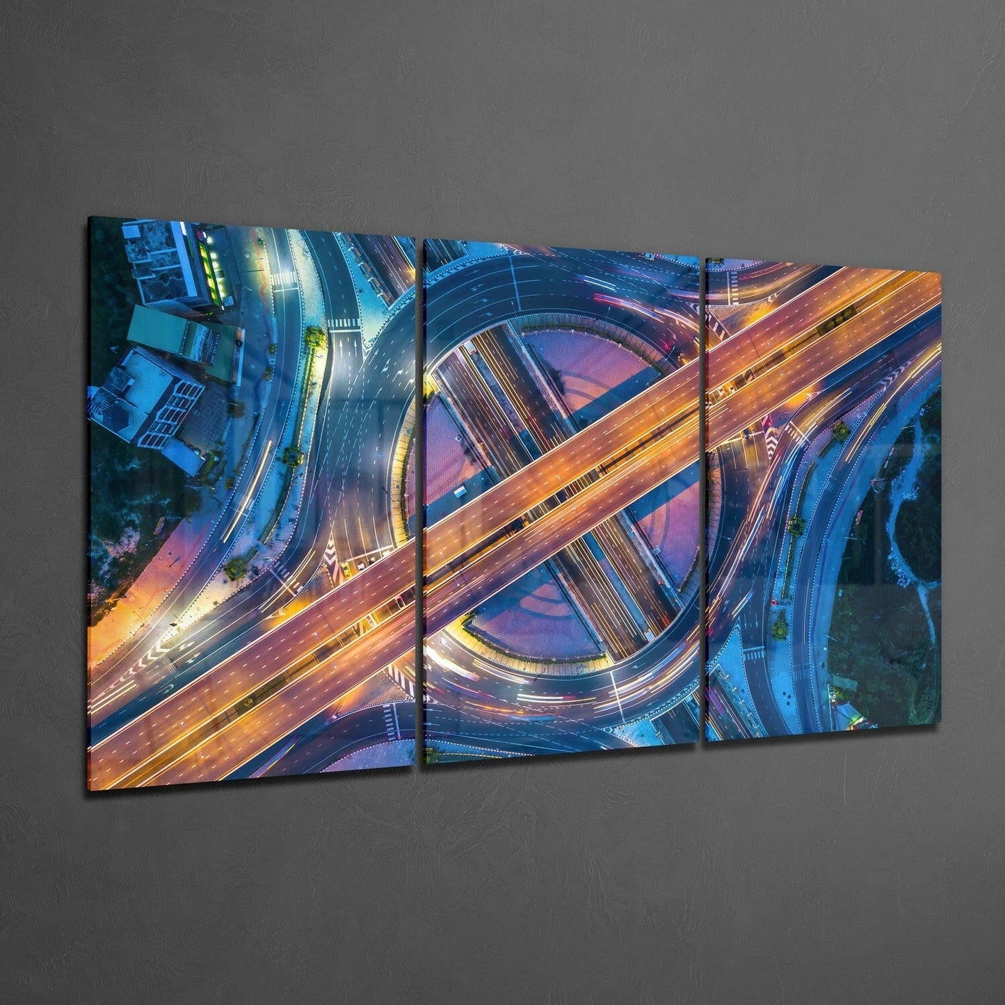 Three-panel glass wall art displaying aerial view of illuminated highway interchanges with golden and blue lighting at dusk.