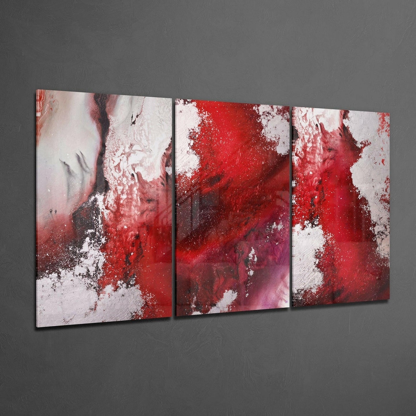 Three-panel abstract glass wall art displaying red, white, and burgundy splatter patterns in an angled display view against gray wall.