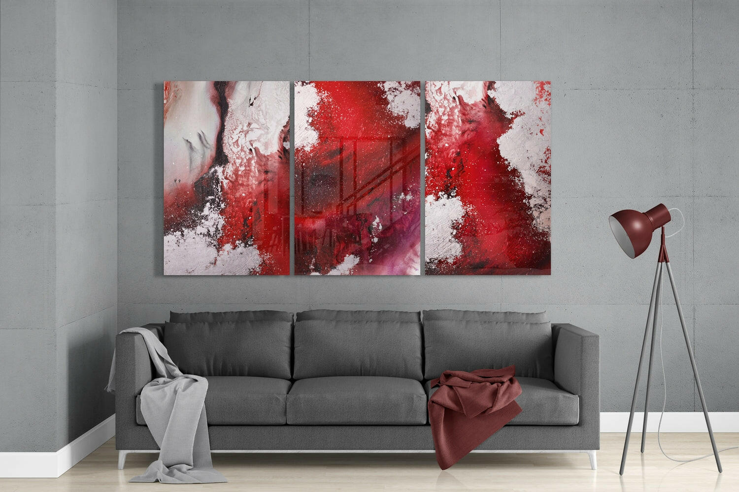 Three-panel abstract red and white glass art hung above gray sofa in modern living room interior.
