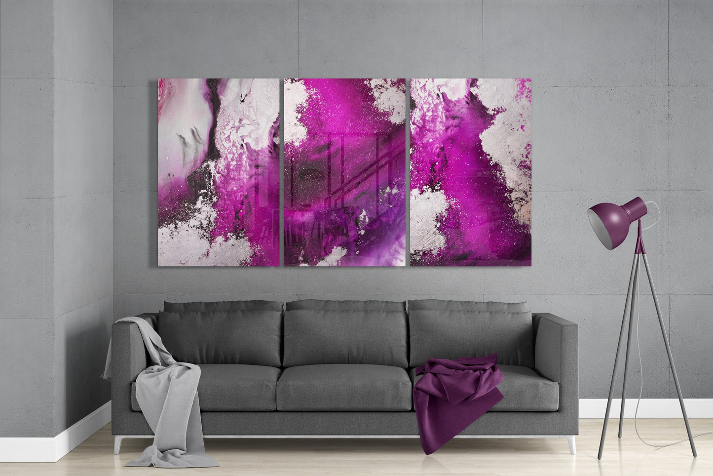 Three-panel fuchsia and white abstract glass art displayed above gray sofa in modern living room setting.