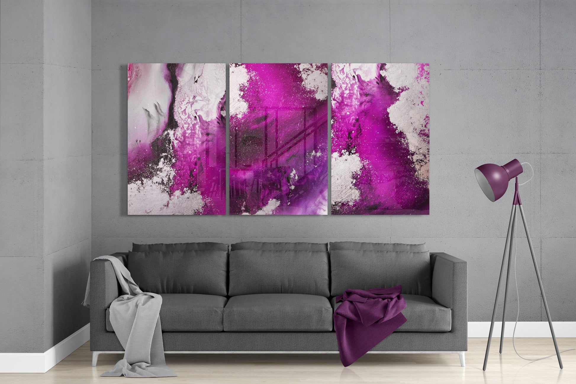 Three-panel fuchsia and white abstract glass art displayed above gray sofa in modern living room setting.