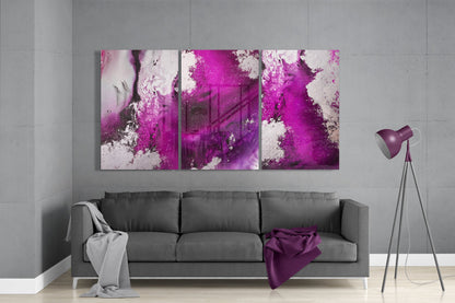 Three-panel fuchsia and white abstract glass art displayed above gray sofa in modern living room setting.