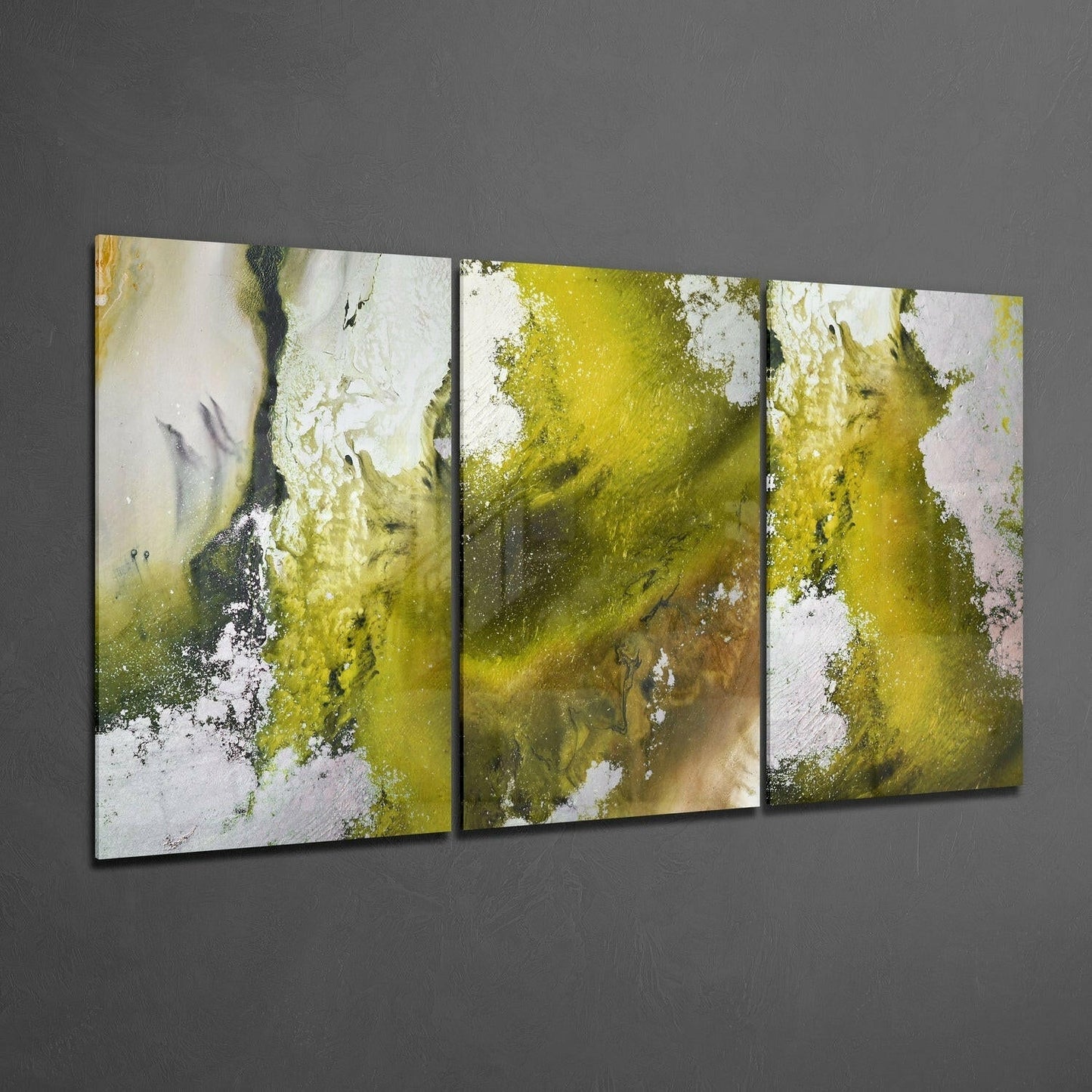 Three-panel abstract glass wall art with yellow-green moss-like patterns and white areas mounted on gray wall, angled perspective view.