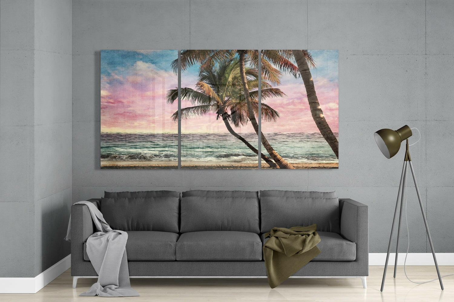 Three-panel glass wall art depicting palm trees on a tropical beach at sunset, displayed above a gray sofa in a minimalist living room.