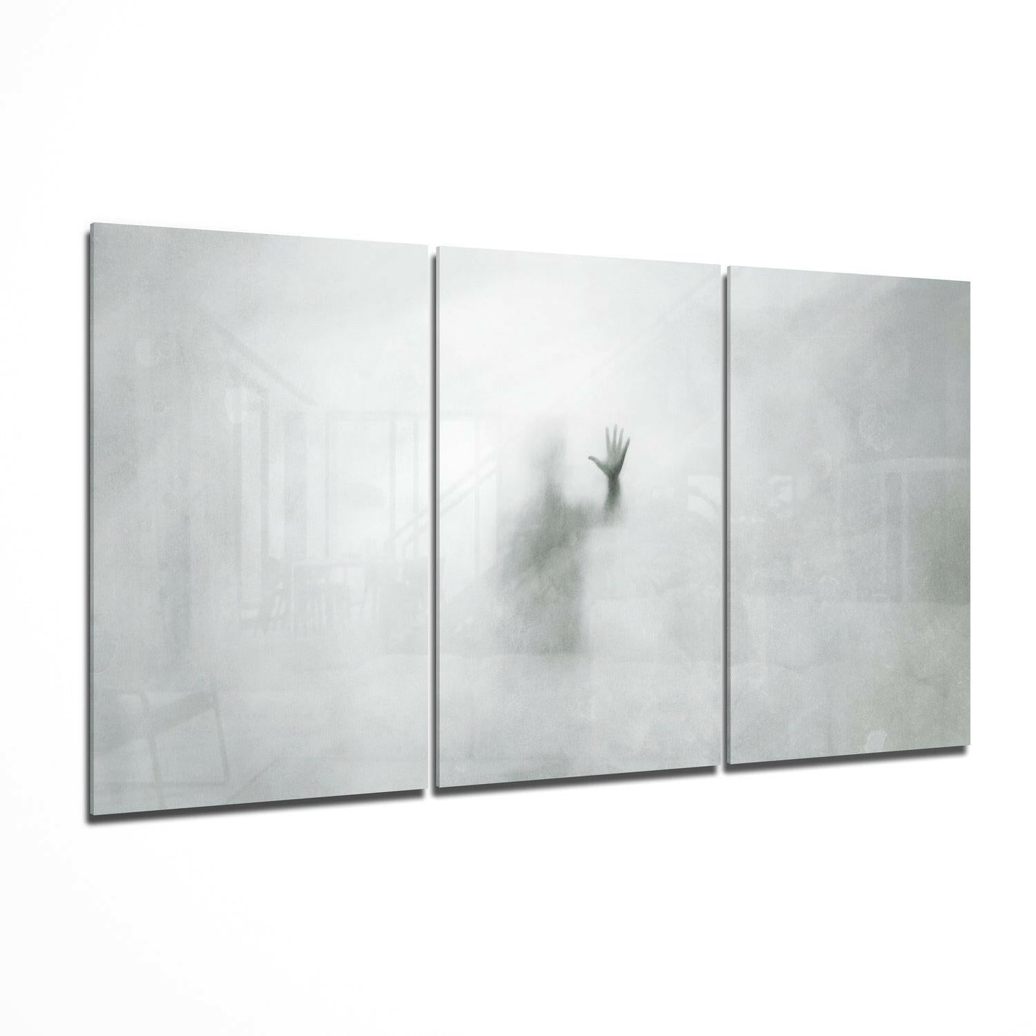 Three-panel glass wall art displaying a blurred silhouette of a figure with raised hand against a misty white background.