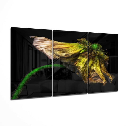 Three-panel black glass wall art displaying a wilting yellow poppy with green stem against dark background, shown at an angle.