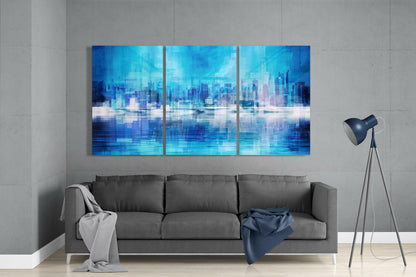 Three-panel blue glass wall art depicting a pixelated cityscape with water reflection, displayed above gray sofa in modern living room.