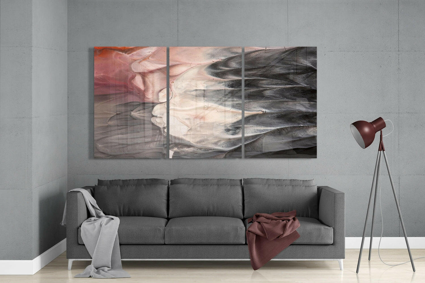 Three-panel abstract glass wall art in muted tones of rose, cream, and charcoal displayed above a gray sofa in a modern living room.