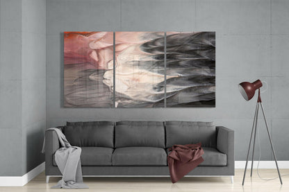 Three-panel abstract glass wall art in muted tones of rose, cream, and charcoal displayed above a gray sofa in a modern living room.