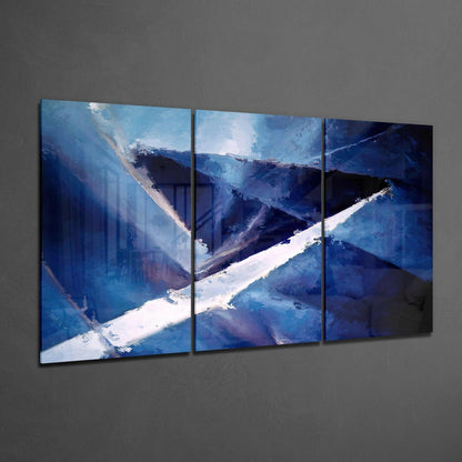 Three-panel sharp blue glass wall art displaying an abstract snowy mountain landscape with white peaks and deep blue valleys against gray wall.