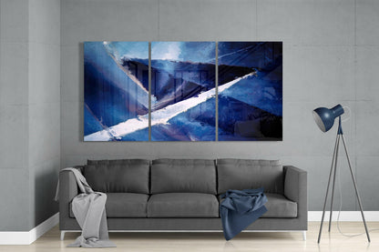 Three-panel blue glass wall art depicting an abstract snowy mountain landscape displayed above a gray sofa in a minimalist living room.
