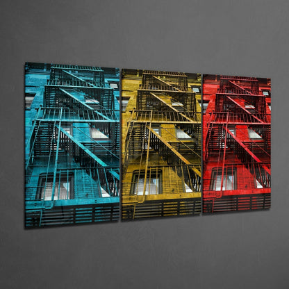 Three glass wall art panels displaying colorful fire escape photographs in blue, yellow, and red tones against gray wall.