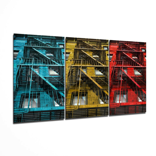 Three triptych glass panels displaying fire escape facades in blue, yellow, and red color treatments against white background.