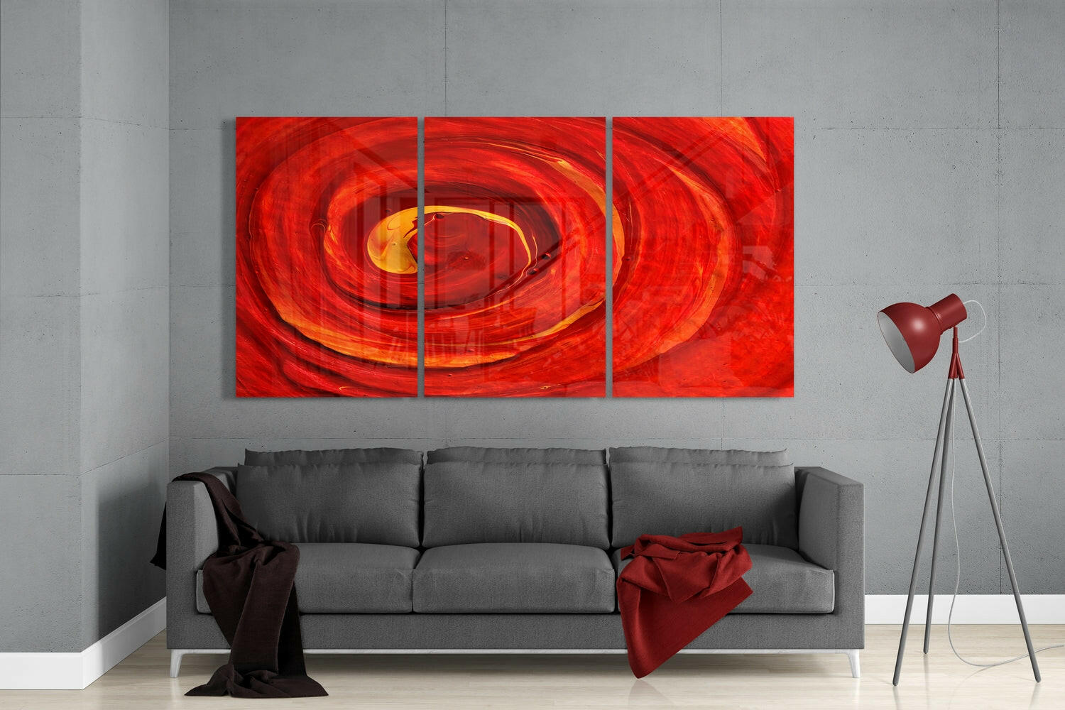 Three-panel red glass wall art with swirling orange and yellow center displayed above gray sofa in modern living room.