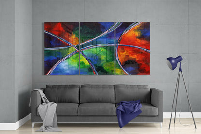 Vibrant multi-panel glass wall art featuring intersecting curved white lines and bold red, blue, green, and orange abstract shapes displayed above a gray sofa.