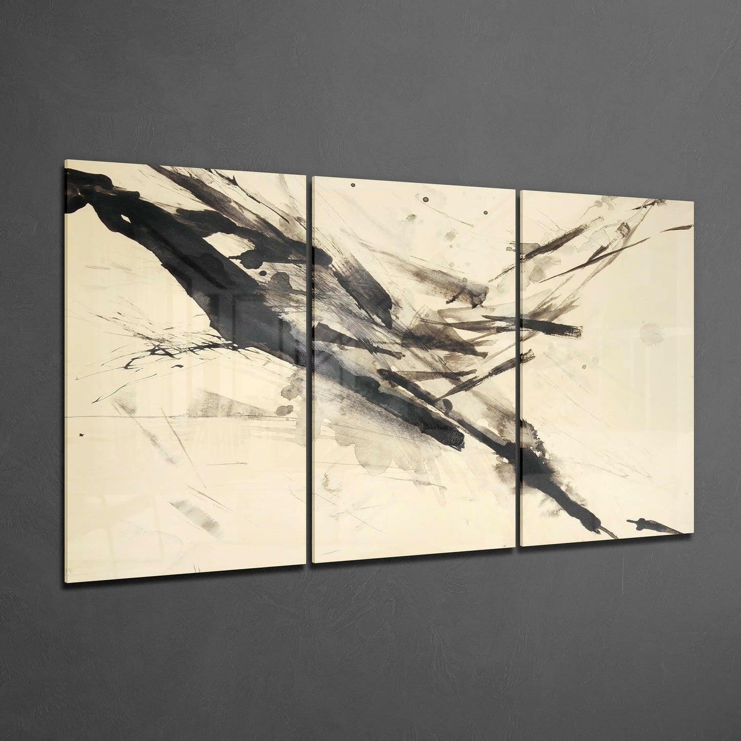 Three-panel glass wall art with abstract black brushstrokes and charcoal marks on cream background, displayed at angle against gray wall.