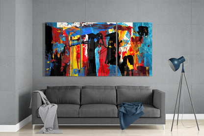 Colorful glass wall art panel with red, blue, yellow, and black abstract silhouettes displayed above gray sofa in modern living room.