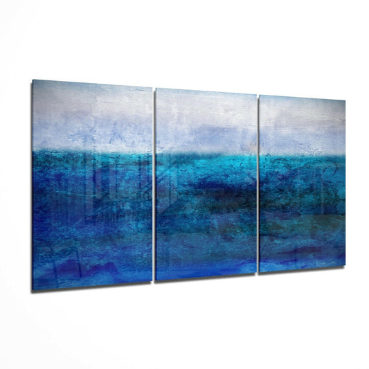 Three-panel glass wall art displaying layered ocean and sky in shades of blue, white, and turquoise with textured brushstrokes.