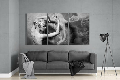 Three-panel black and white glass wall art mounted above gray sofa, depicting artistic figure with flowing fabric and raised arms.