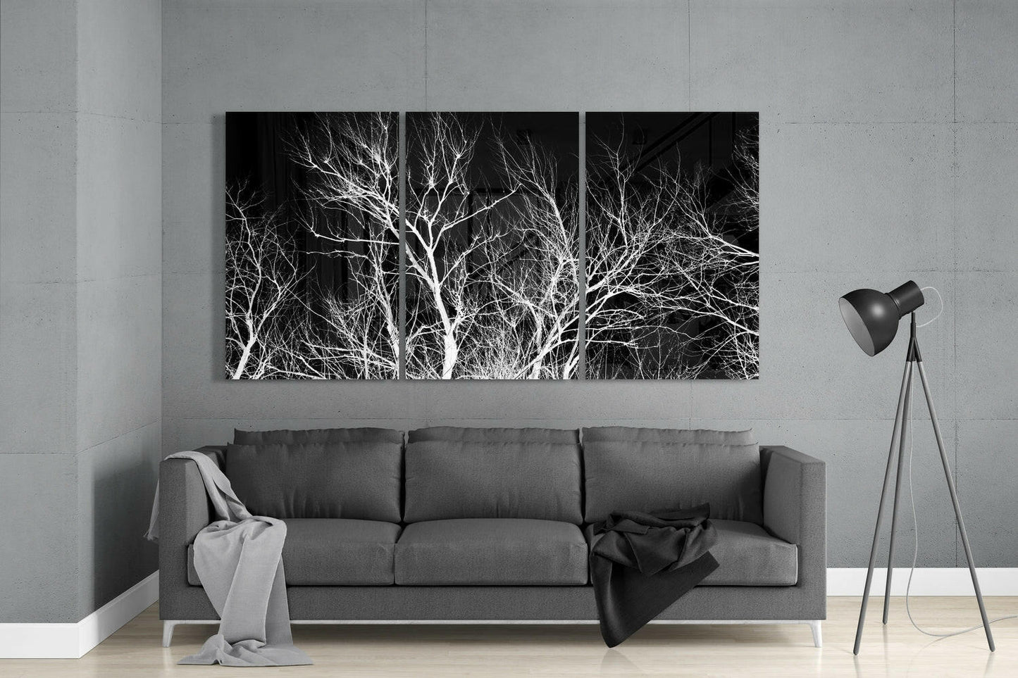 Three-panel black and white glass wall art displaying bare tree branches above a gray sofa in a minimalist living room.