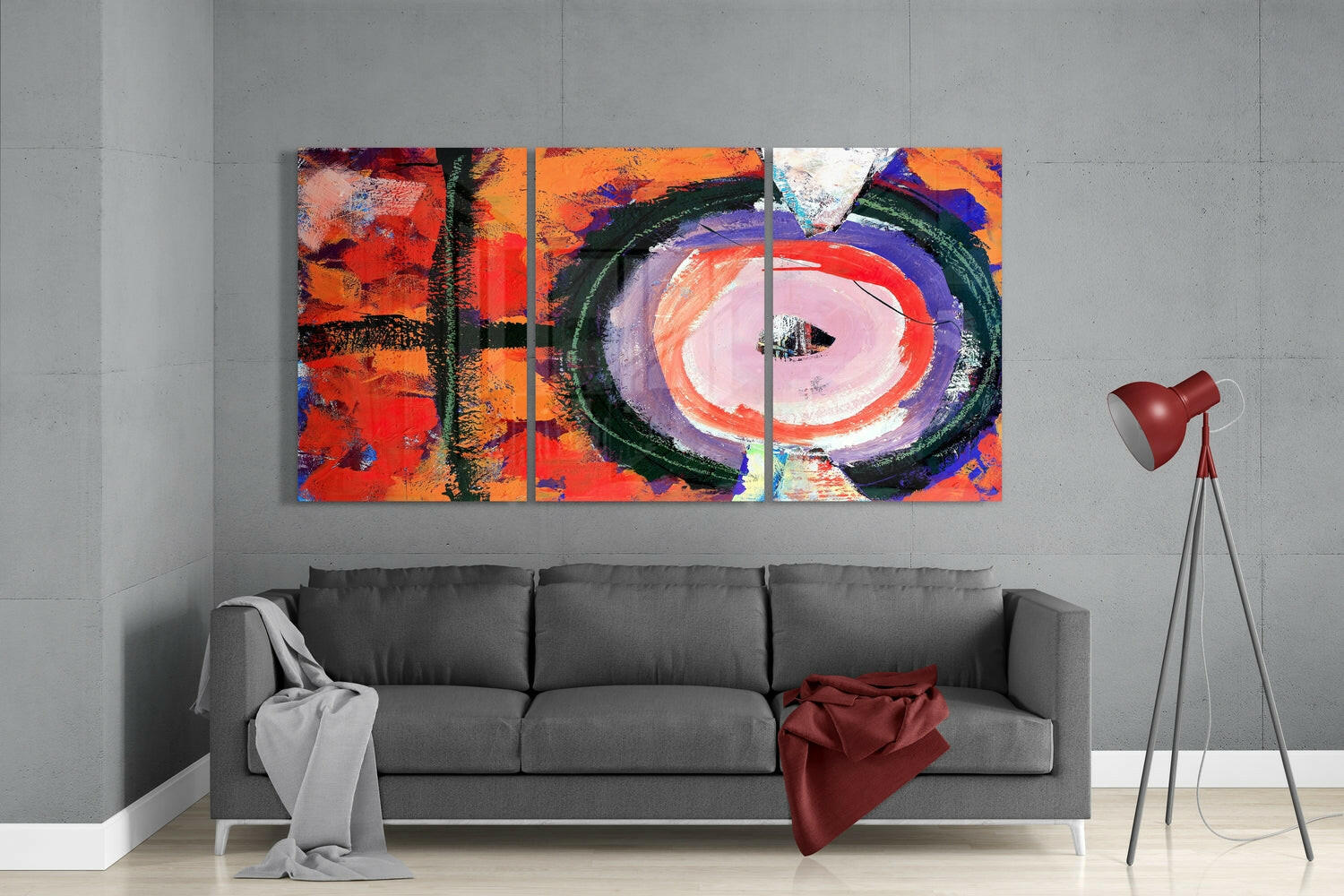 Three-panel colorful glass wall art with red, orange, and purple abstract design mounted above gray sofa in modern living room.