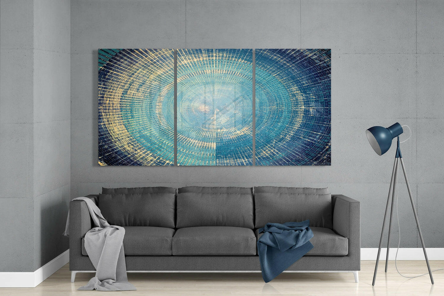 Three-panel glass wall art with concentric circular pattern in blue, teal, and gold tones displayed above gray sofa in modern living room.