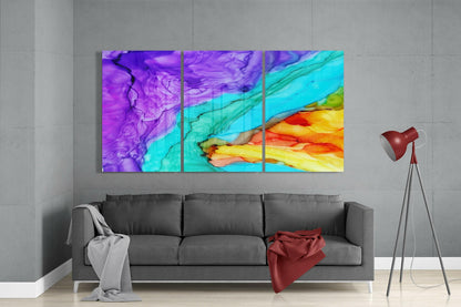 Triptych glass wall art with swirling purple, turquoise, yellow, and orange ink patterns displayed above gray sofa in modern living room.