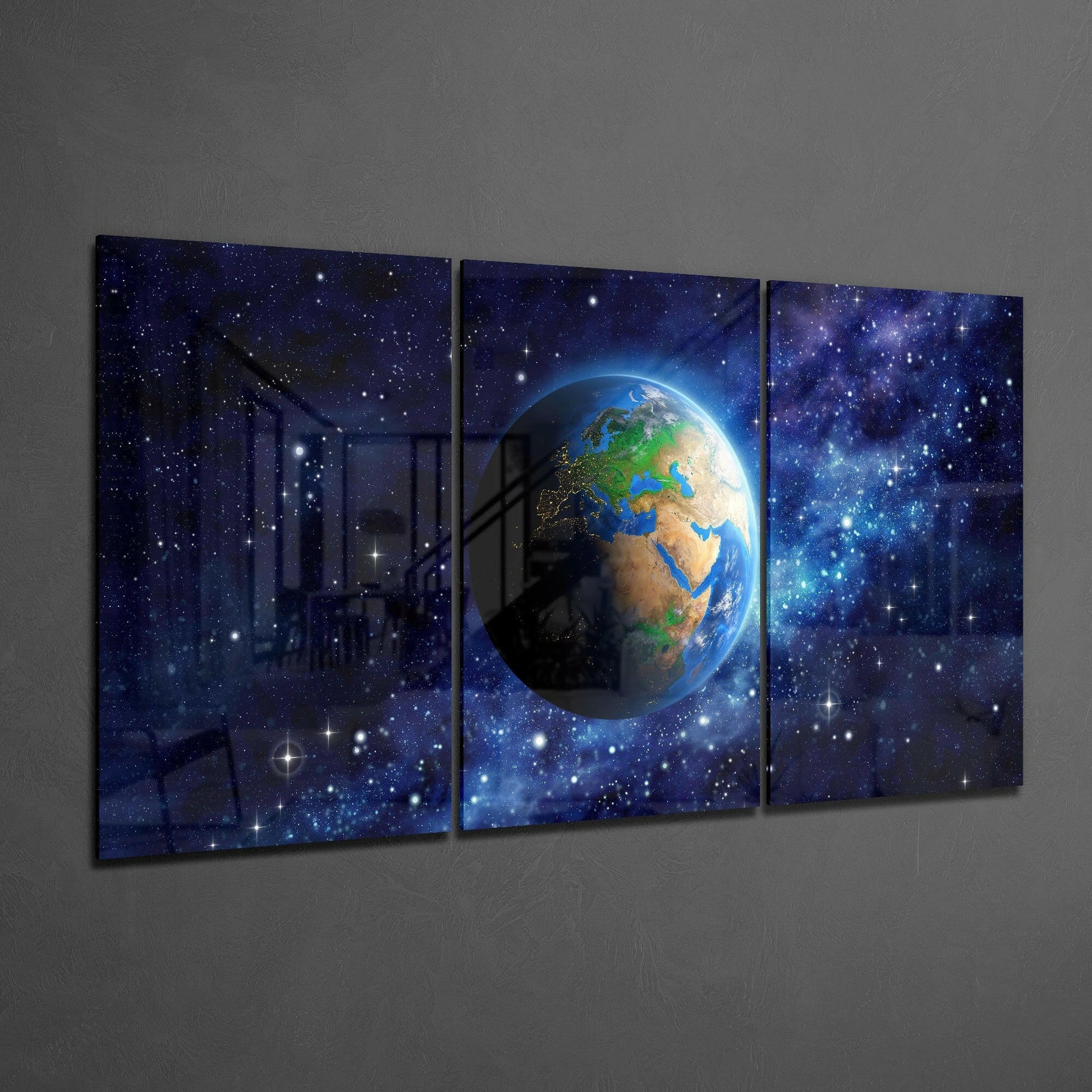 Three-panel glass art displaying Earth centered against a starry blue space background, hung on gray wall.