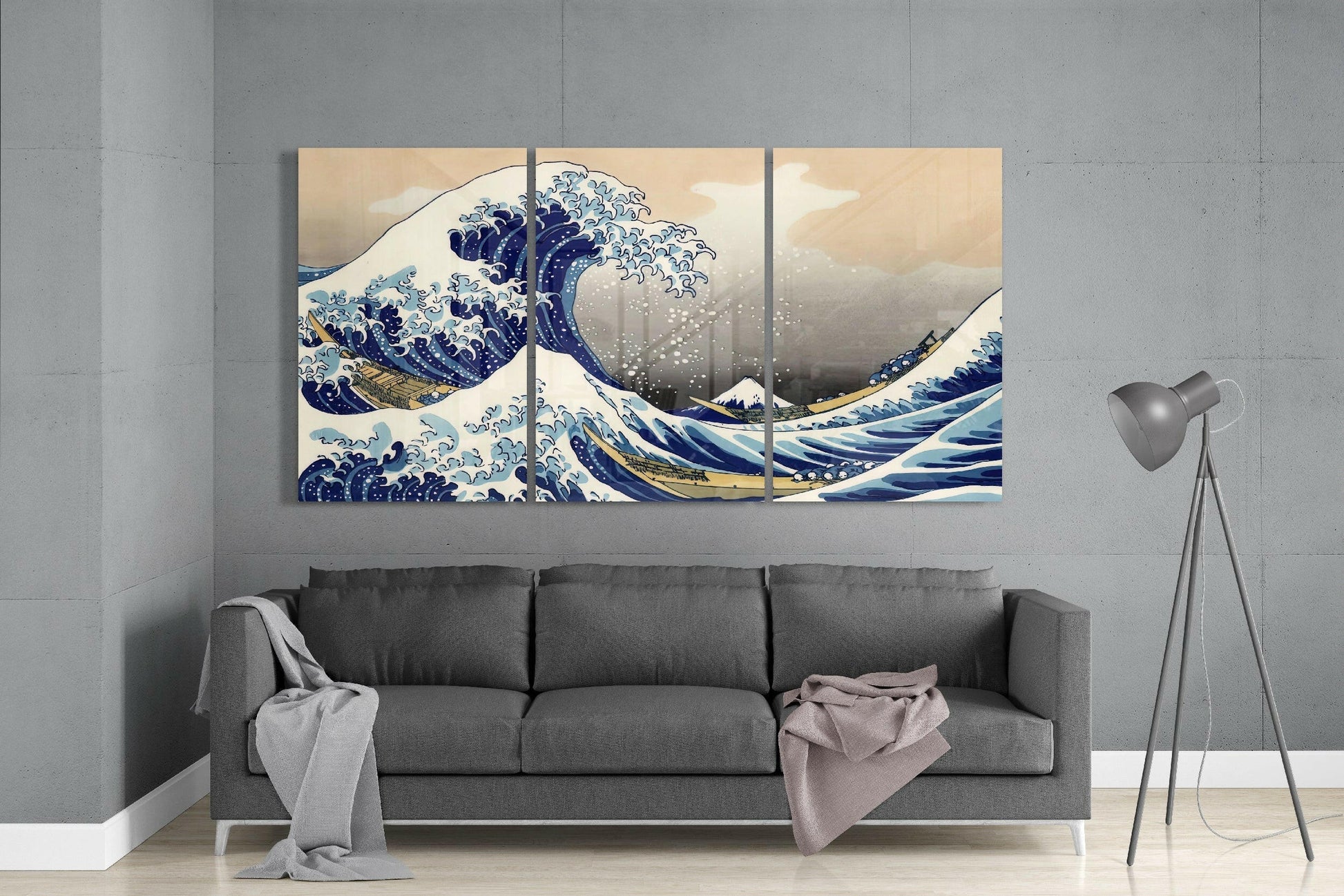 Three-panel glass art displaying Hokusai's Great Wave in blue and cream tones mounted above a gray sofa in a modern living room.
