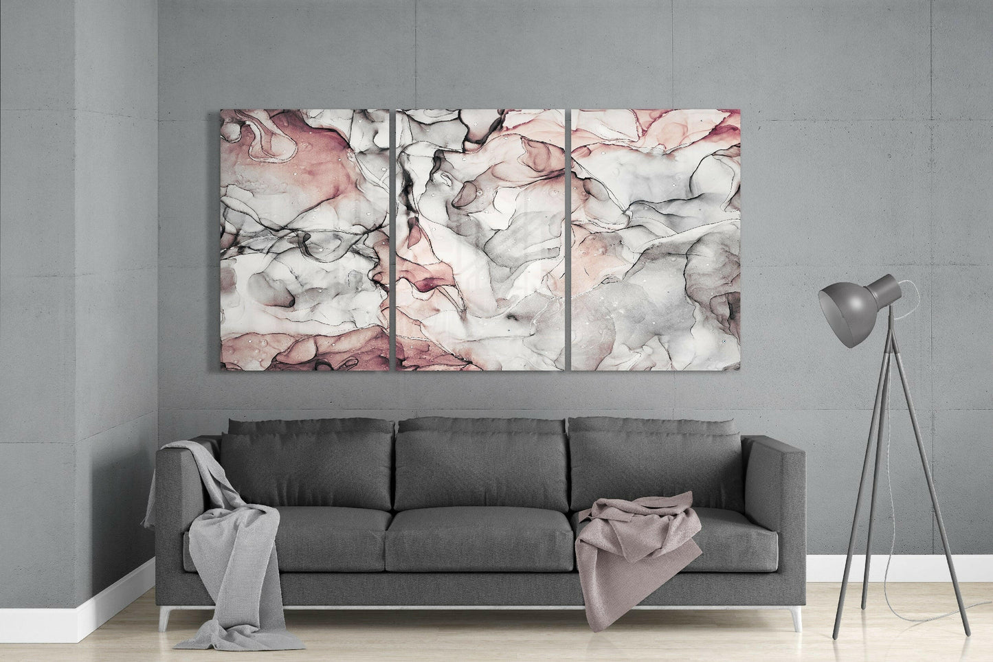 Three abstract glass art panels with pink, gray, and black marbled patterns mounted above a gray sofa in a modern living room.