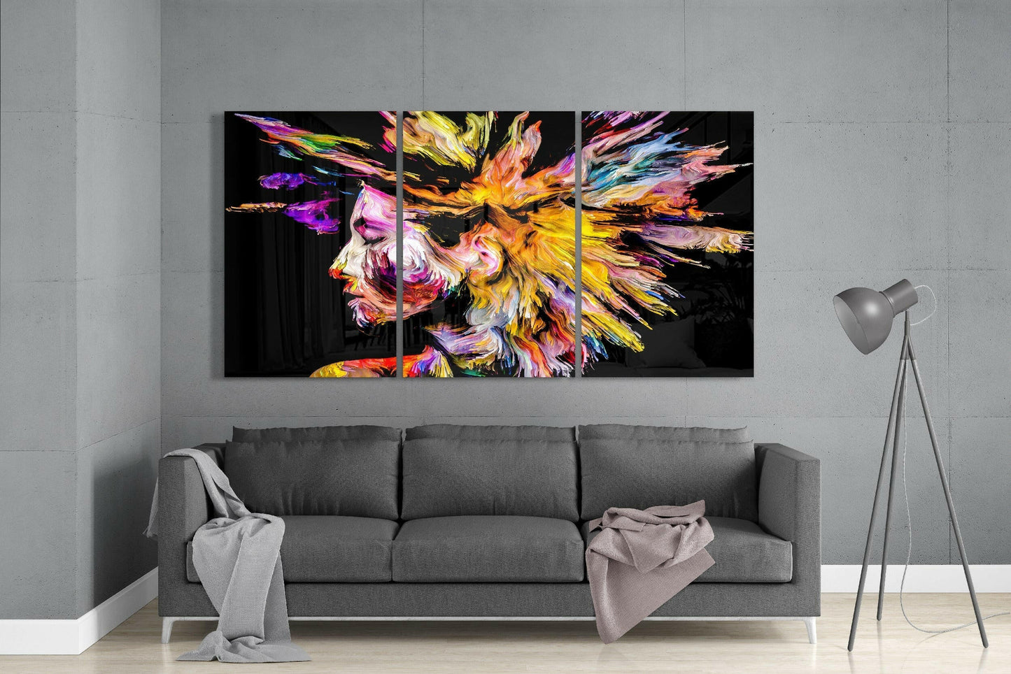 Colorful Thoughts glass art triptych displaying an abstract lion profile in vibrant yellows, purples, pinks, and blues against black, mounted above a gray sofa in a modern living room.