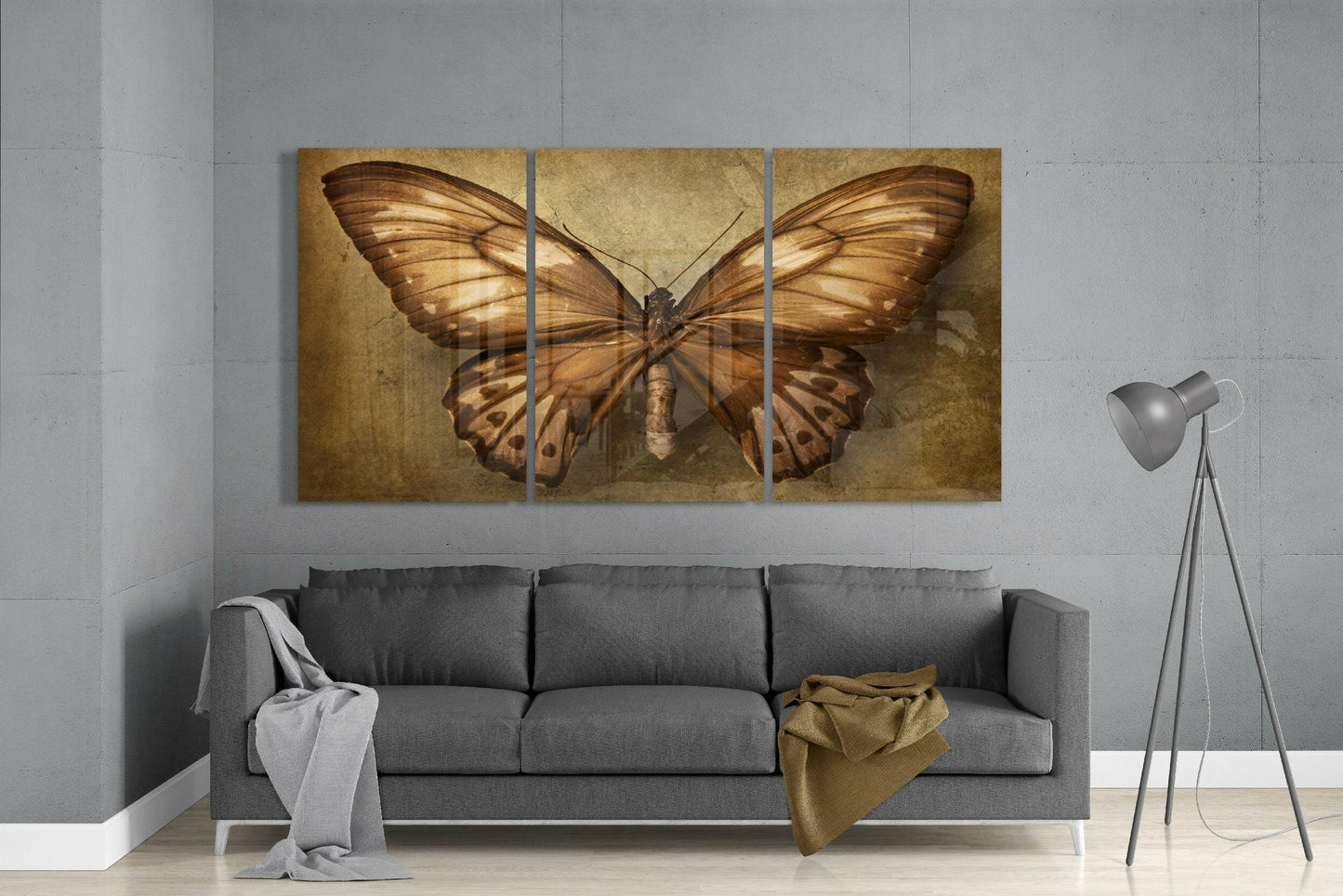 Three-panel bronze butterfly glass art displayed above gray sofa in modern living room interior.
