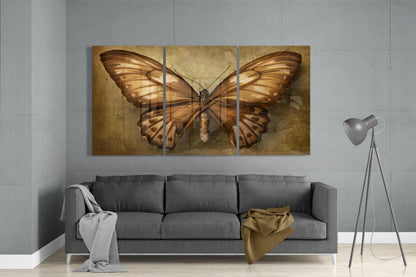 Three-panel bronze butterfly glass art displayed above gray sofa in modern living room interior.