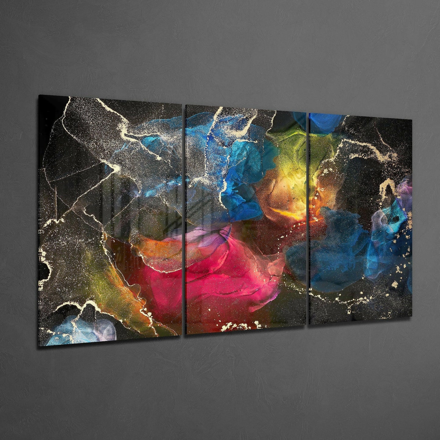 Multi-panel glass art displaying vibrant splashes of pink, blue, yellow, and gold with white sparkle accents on dark background, hung on gray wall.
