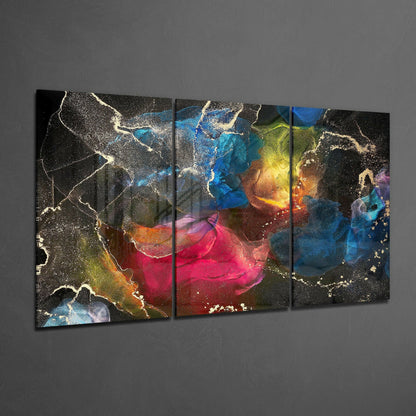 Multi-panel glass art displaying vibrant splashes of pink, blue, yellow, and gold with white sparkle accents on dark background, hung on gray wall.