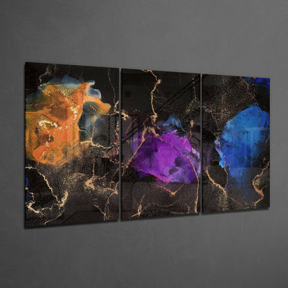 Three-panel glass art display featuring abstract watercolor designs in orange, purple, and blue with gold leaf accents on black backgrounds, shown at an angle against a gray wall.