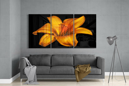 Three-panel orange lily glass art displayed above a gray sofa in a minimalist living room setting.