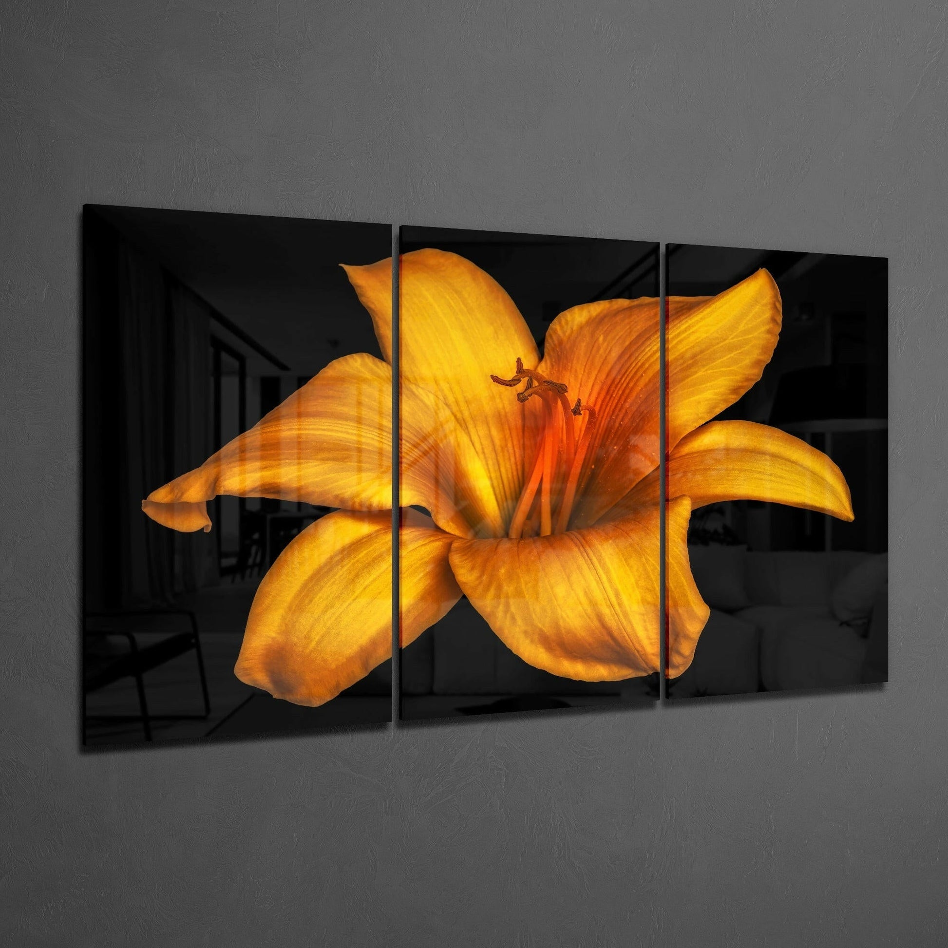 Three-panel glass art displaying a vibrant orange lily with yellow petals against black background, mounted on gray wall.