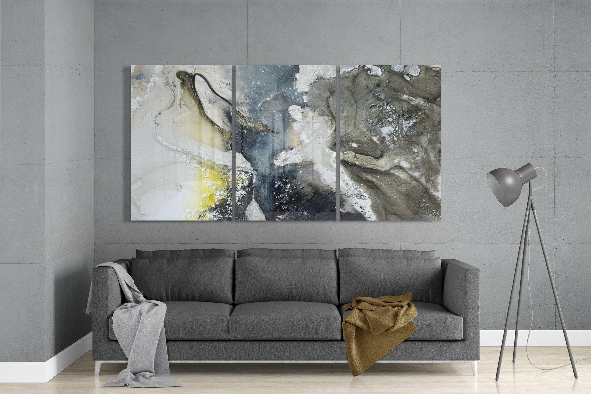 Three-panel abstract glass art with white, grey, and earth-tone textures displayed above grey sofa in modern living room.