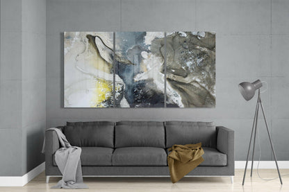 Three-panel abstract glass art with white, grey, and earth-tone textures displayed above grey sofa in modern living room.