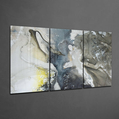 Three-panel glass art display showing abstract textured surfaces with white, gray, yellow, and blue tones against dark wall.
