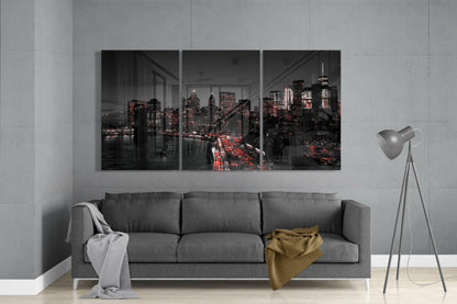 Three-panel glass art depicting a nighttime cityscape with illuminated buildings and red traffic lights, displayed above a gray sofa in a modern living room.