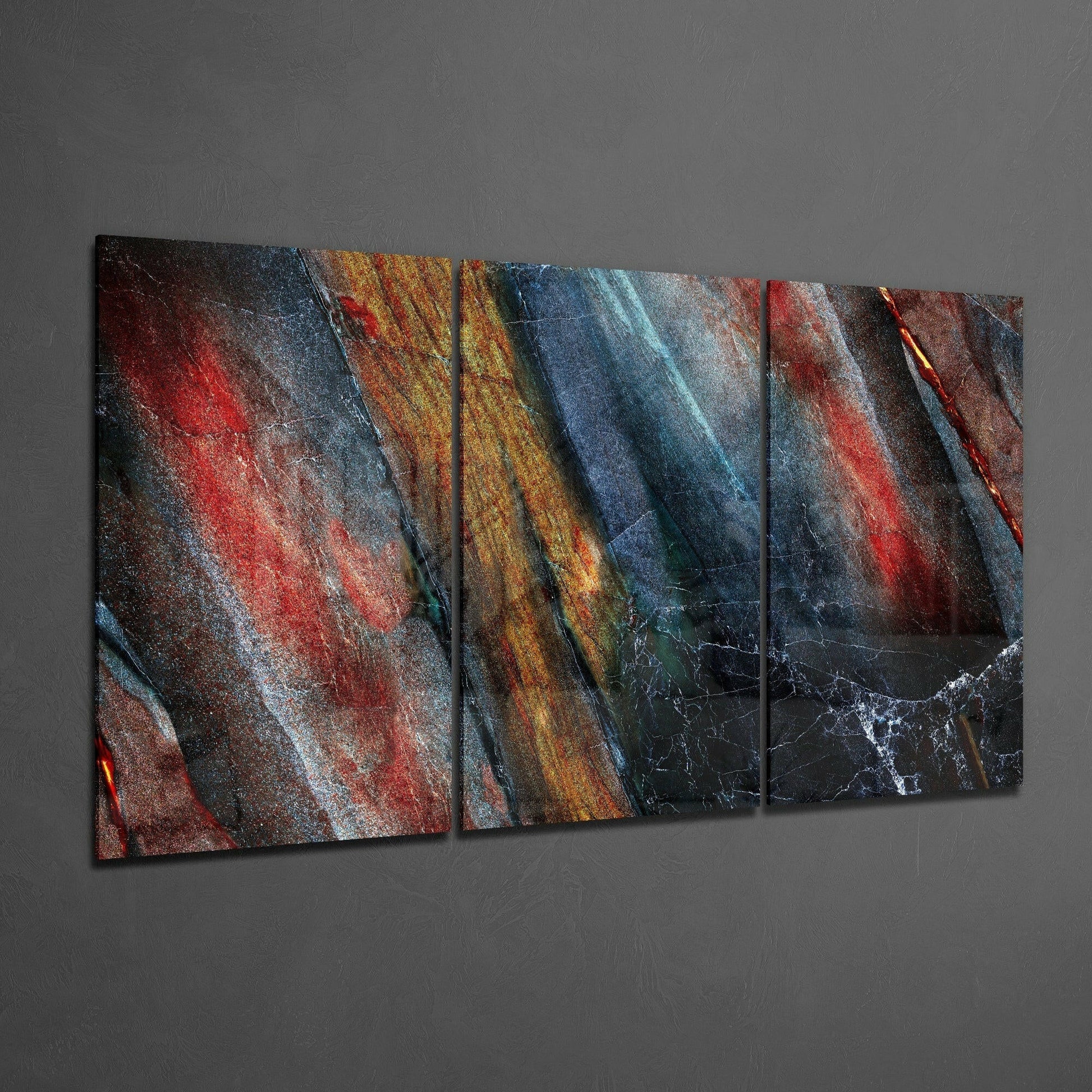 Three-panel glass art display featuring layered diagonal stripes in red, gold, blue, and black with textured surfaces mounted on gray wall.
