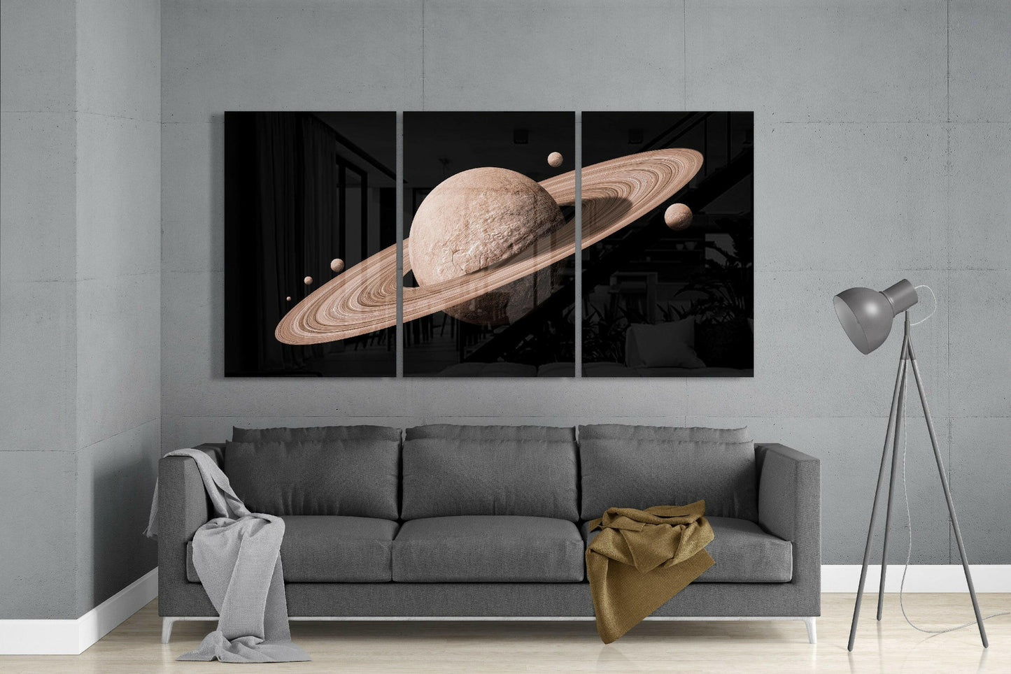 Three-panel Saturn glass art installation above gray sofa displaying tan planet with rings and moons against black background.