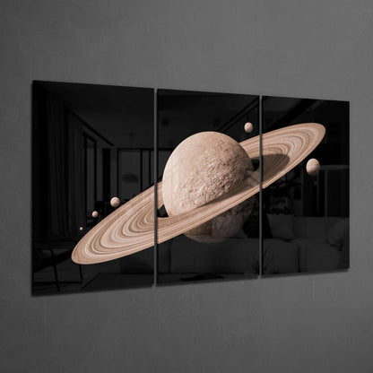 Three-panel glass art depicting a tan planet with rings and smaller moons against black background, displayed on gray wall.